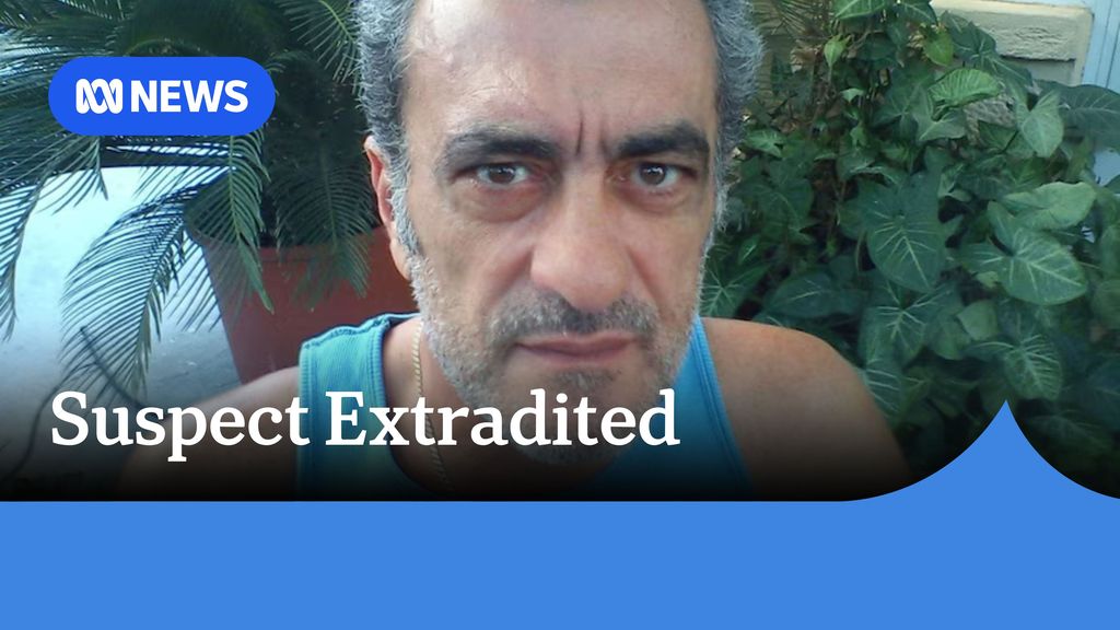 Suspect Extradited: A man with grey hair and facial hair with a light blue singlet.