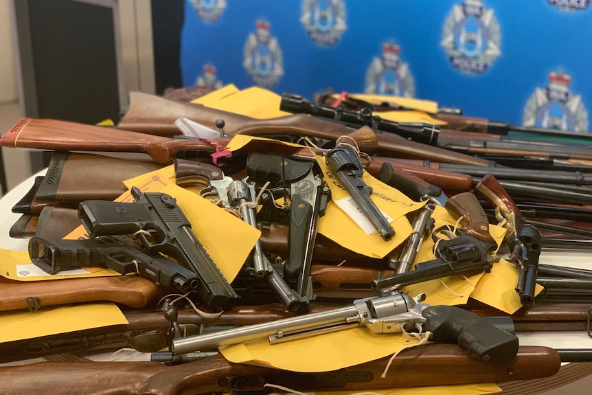 Pile of pistols and rifles on table with police crest in the background