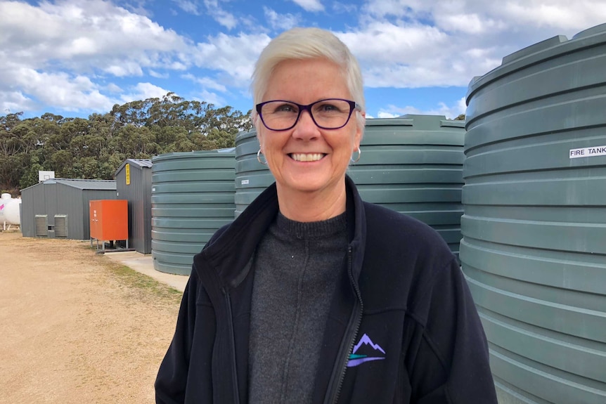 Principal Robyn Francis smiles at the camera, standing in front of water tanks.