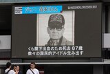 A black-and-white photo of an older man, wearing a cap and dark glaasses, on a billboard with Japanese writing