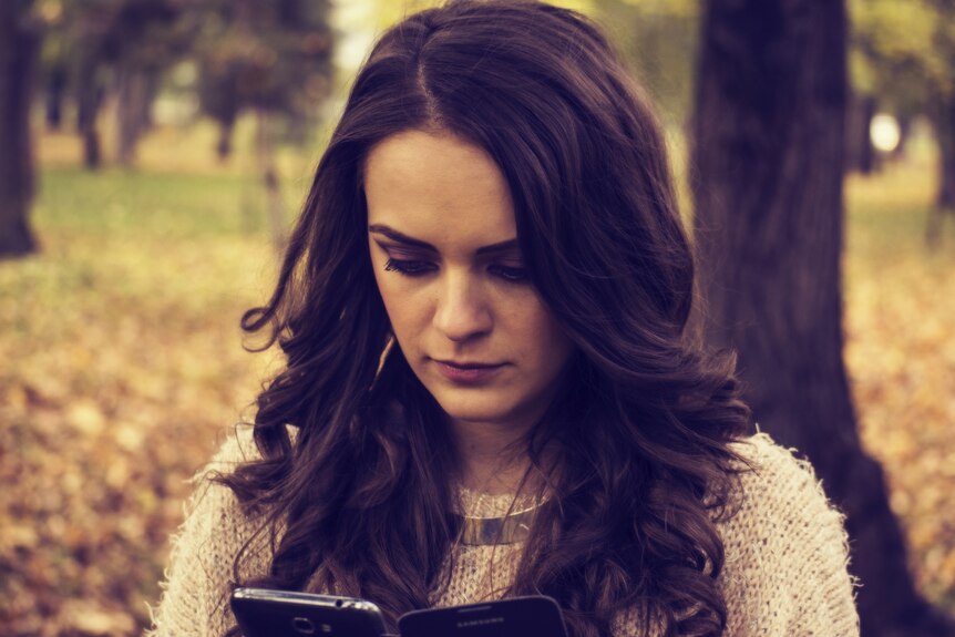 A woman stands outside looking down at her phone with a concerned expression