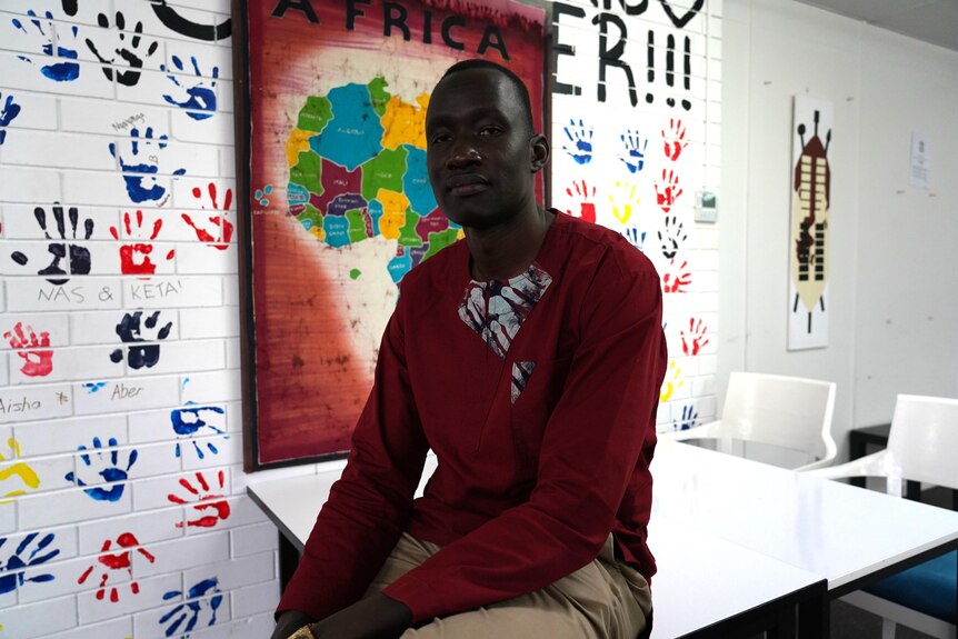 Beny Bol OAM sits in front of a map of Africa