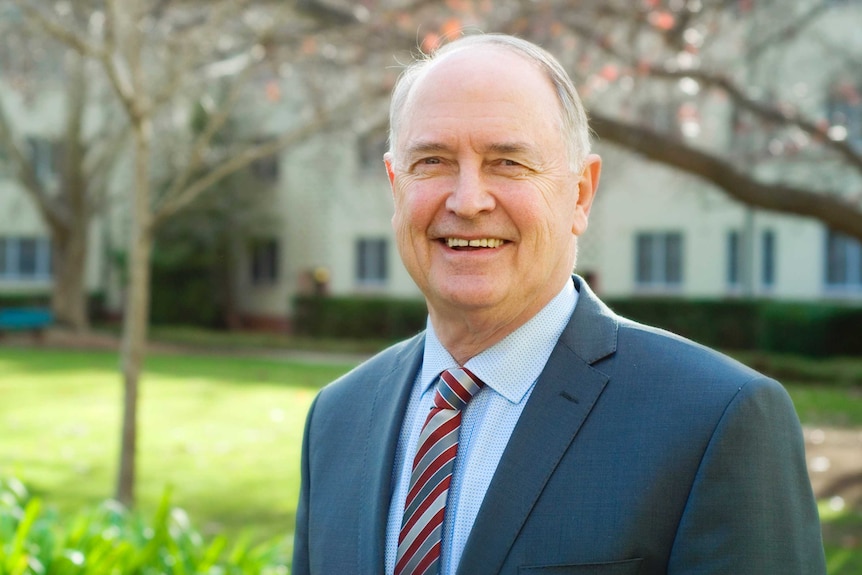 An older man in a suit stands outside, smiling.