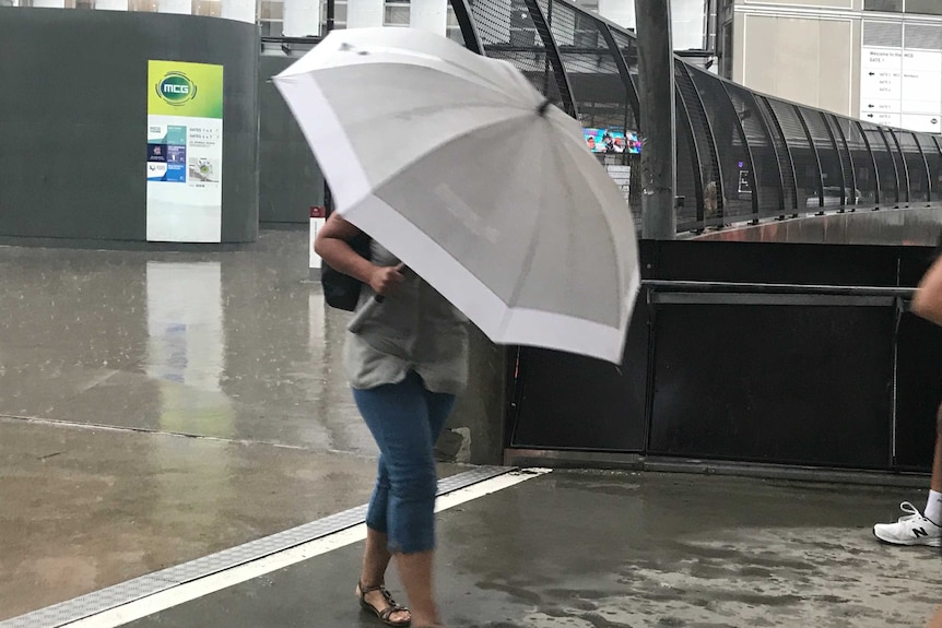A woman hides under an umbrella in heavy rain.