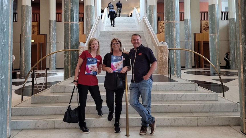 Three people standing together in the foyer of a government building.