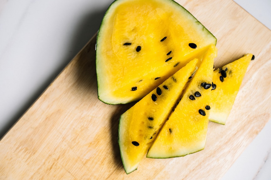 A piece of cut watermelon with yellow flesh and seeds.  