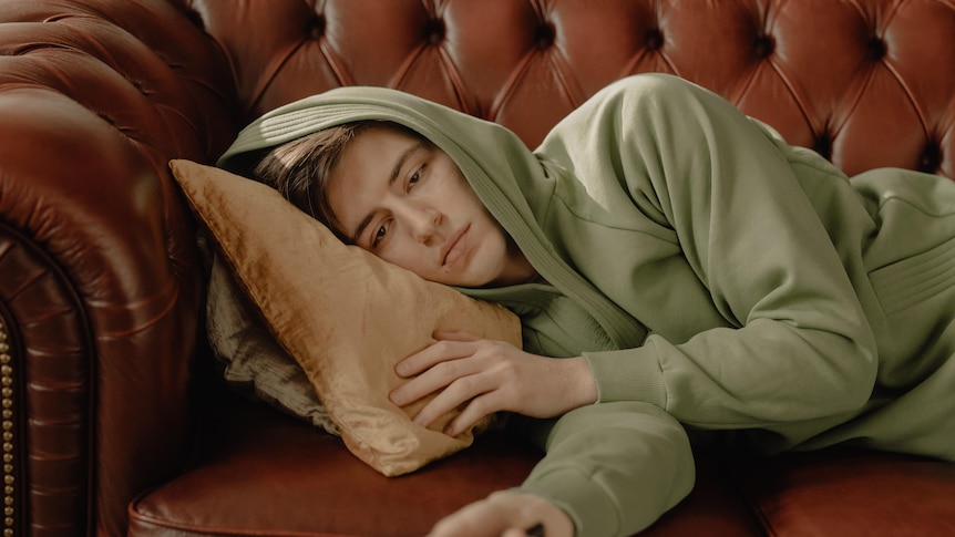 A young man lying on the couch looking depressed