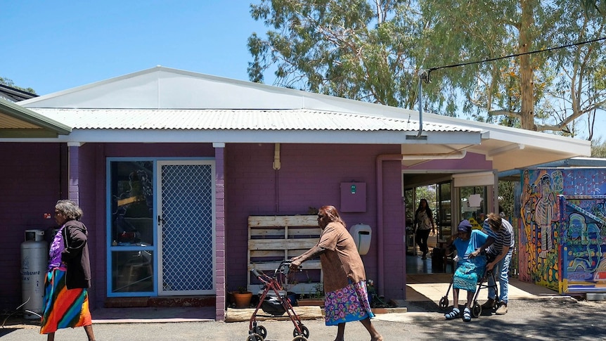 Three Indigenous women, two with walkers, walk past the exterior of a purple house