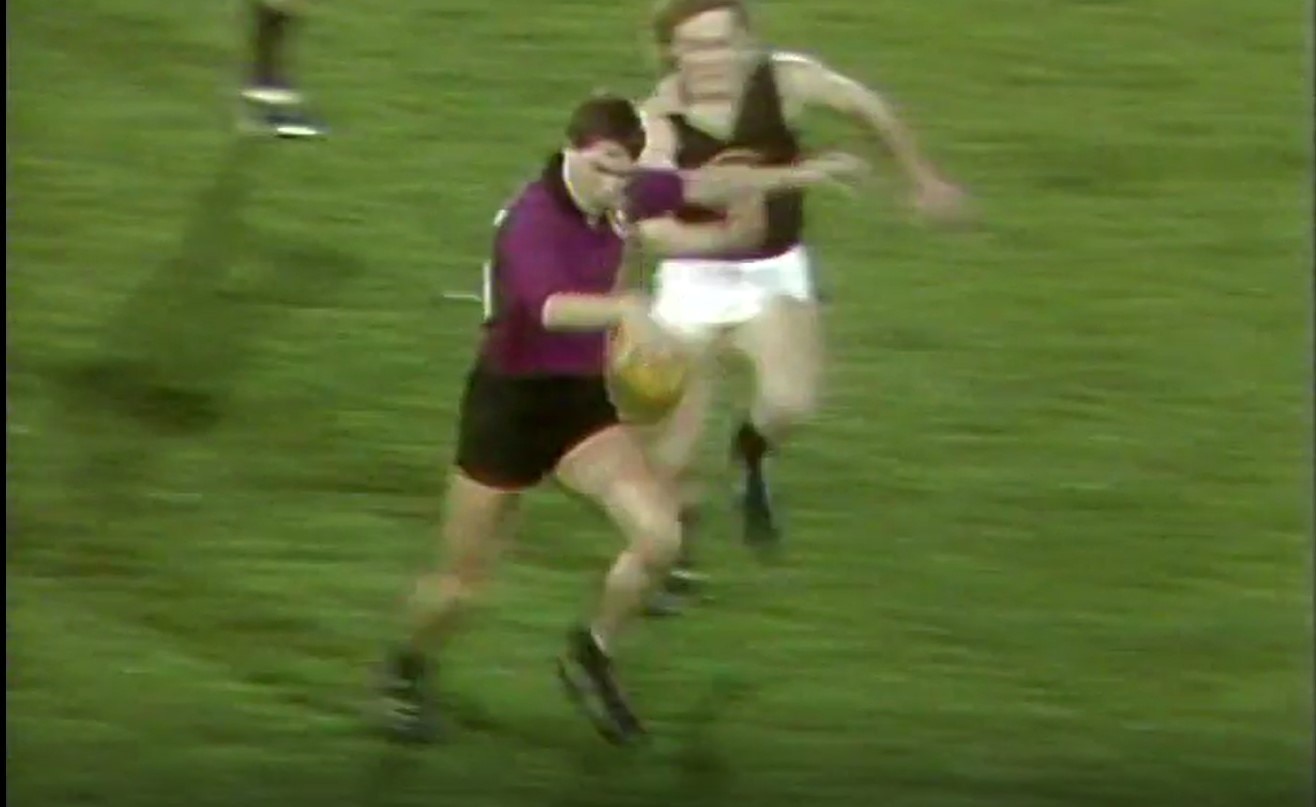 A grainy image of a young footballer in the process of kicking the ball.