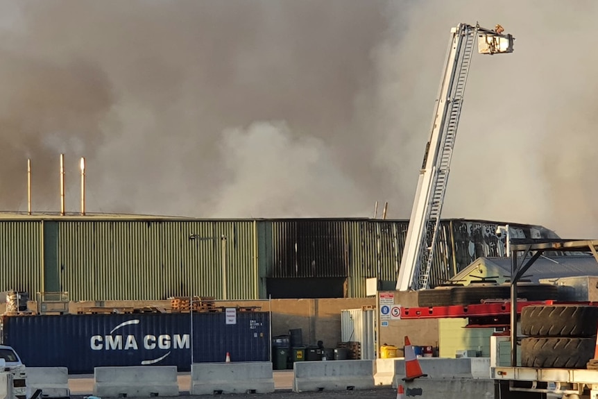 A fire fighting crane shoots water into a burning factory billowing smoke