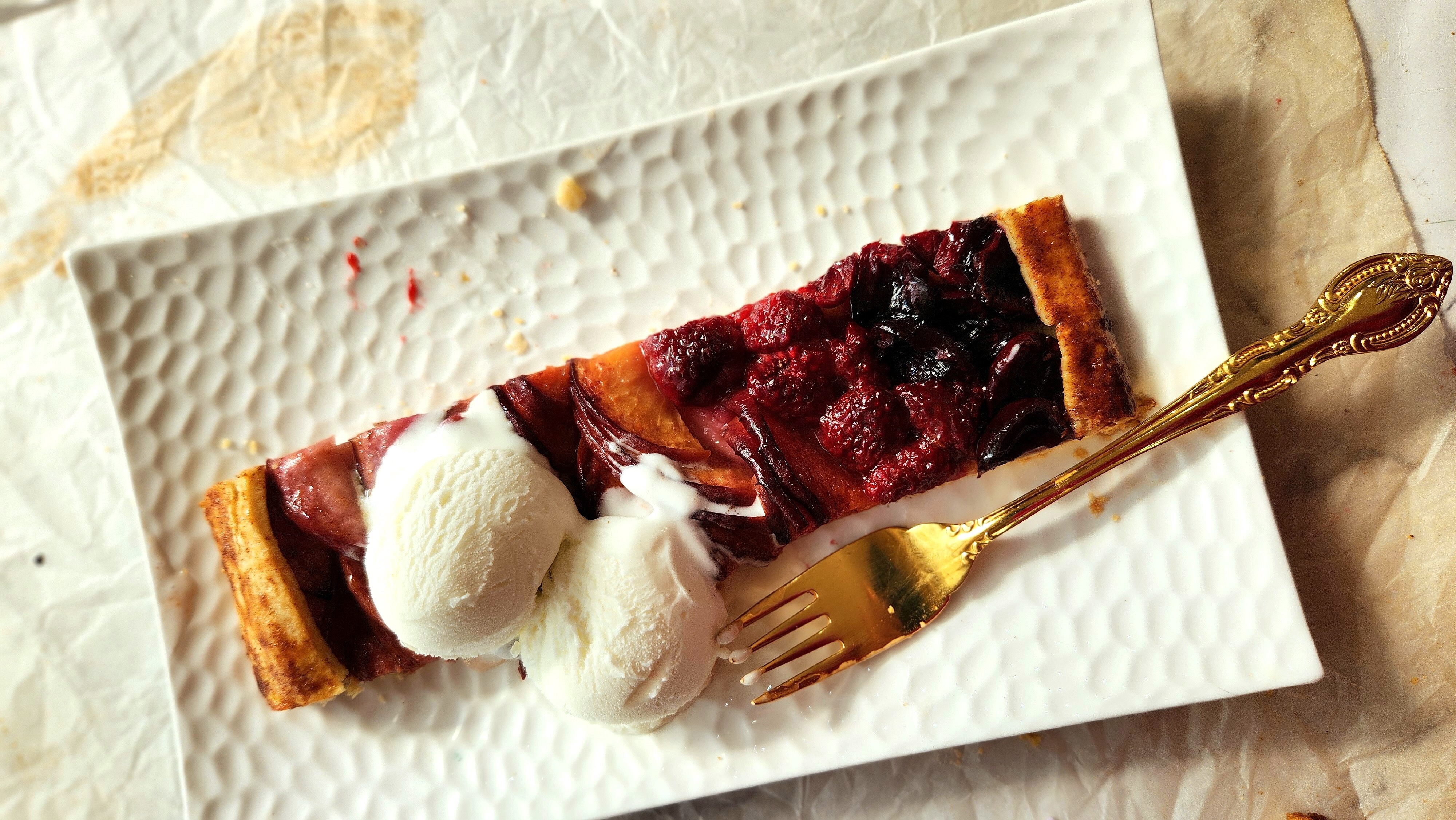A slice of summer fruit galette on a plate with two small scoops of vanilla ice cream.