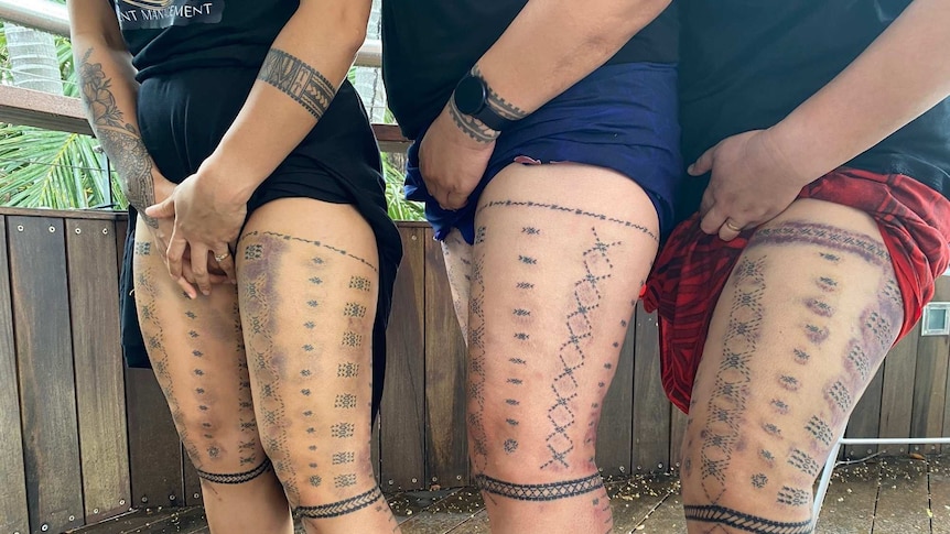 The black lines and designs of traditional malu tattoos are displayed on the legs of three women