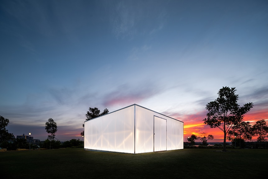 Colour photo of architect-designed pavilion Blak Box, glowing brightly on Stargazer's Lawn as the sunsets at Barangaroo Reserve.