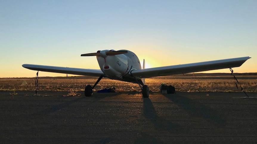 A plane in a field with the sun setting behind it.