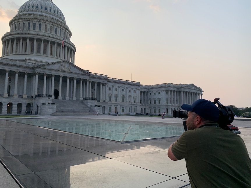 Cameraman filming Capitol Building at sunset.