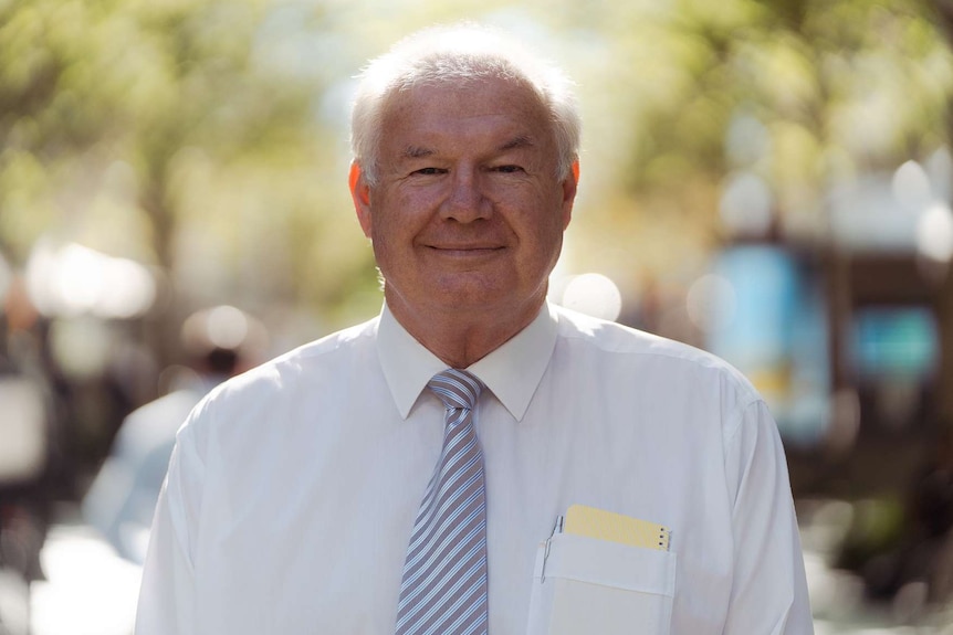 A mid shot of a smiling Brian Childs standing outside in a white business shirt and striped tie.