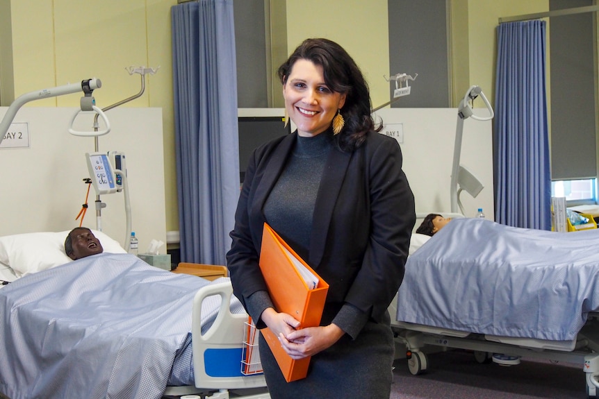 a woman stands in a teaching ward holding an orange binder