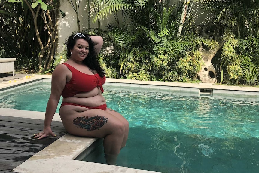 Ally Garrett posing in a red bikini by a pool and smiling