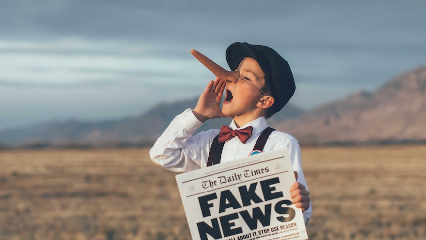 A child with a pinocchio nose holds a newspaper reading 'fake news'.