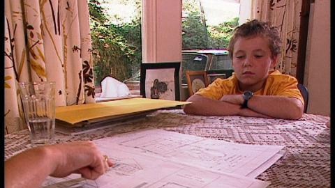 Boy sits at table and looks at a hand pointing to architectural drawings of house