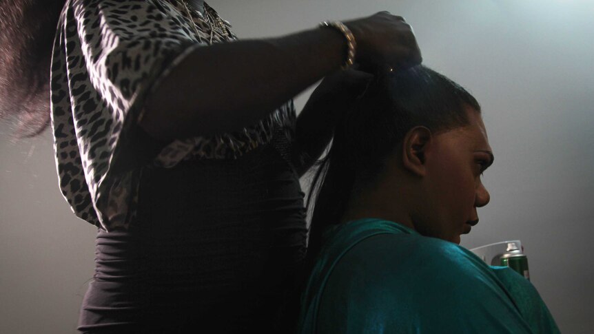 A photo of Shaniqua sitting down as her friend Hot Lips does her hair.
