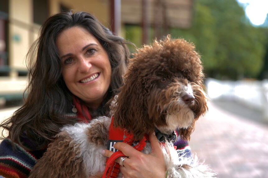 Woman with brown hair smiling holding a shaggy dog. 