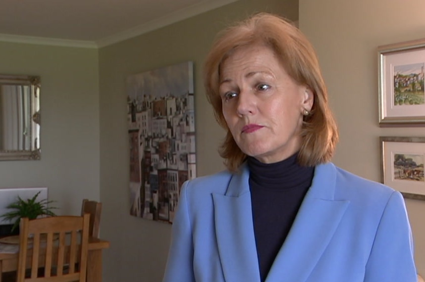 Christine Allen wearing a blue blazer in the living room of a house with paintings on the wall in the background.