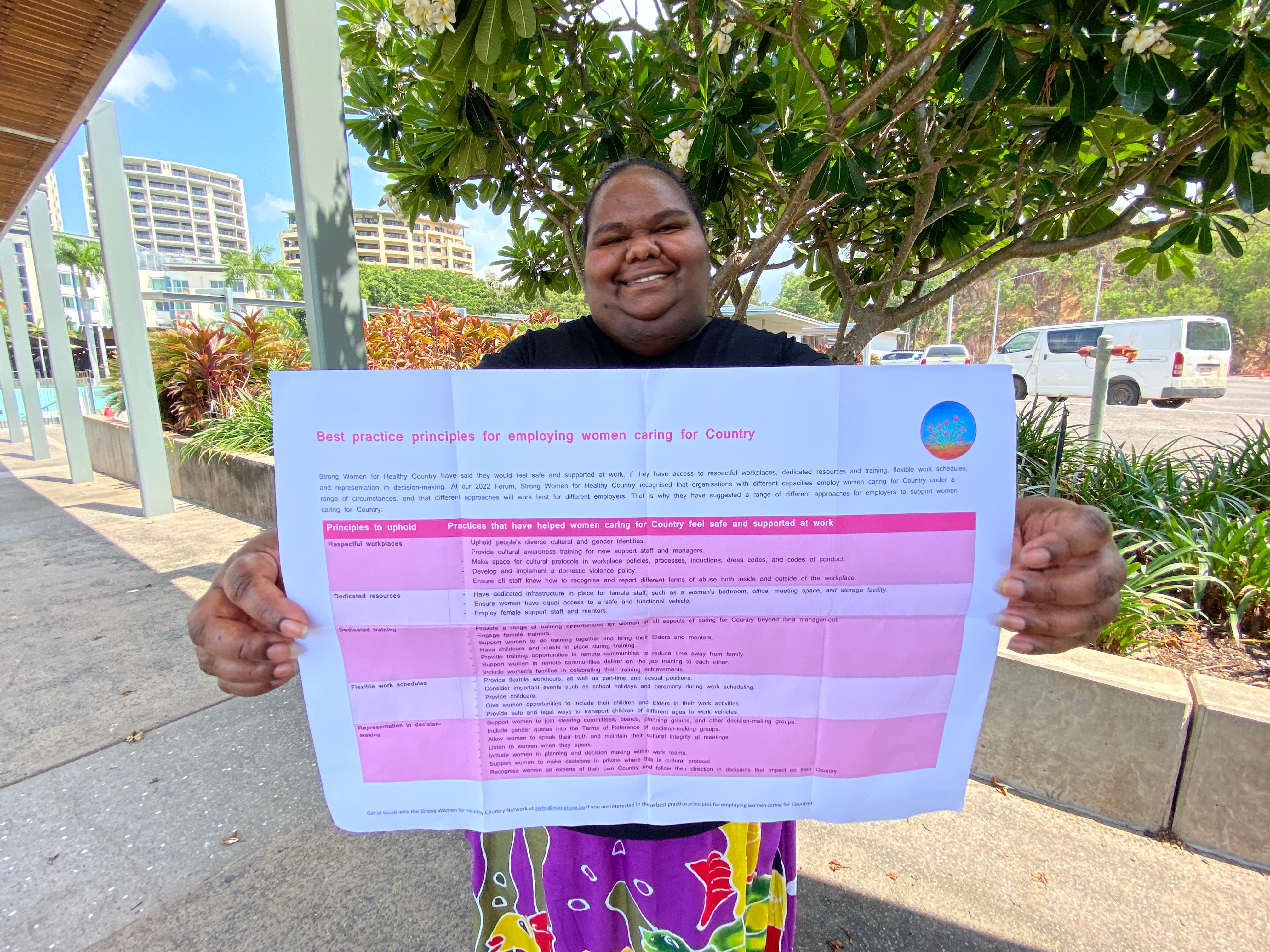 An Aboriginal woman holds a document with a pink table out in front of her. The document is the best practice principles.