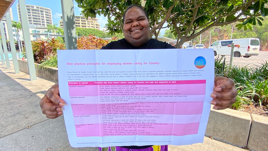 An Aboriginal woman holds a document with a pink table out in front of her. The document is the best practice principles.