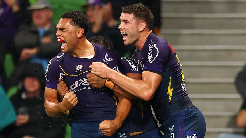 Three Melbourne Storm NRL players embrace as they celebrate a try.