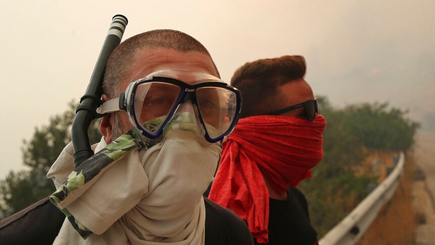 Two men wear cloths over their mouth and nose, with one also wearing a snorkelling mask and snorkel