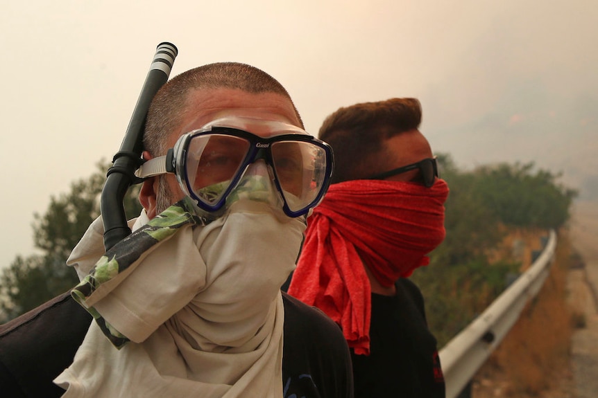 Two men wear cloths over their mouth and nose, with one also wearing a snorkelling mask and snorkel