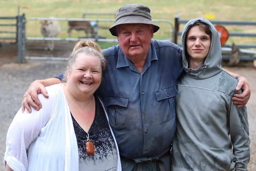 Magda Szubanski smiles next to Egg Boy and farmer in a dirty work shirt on a cattle farm