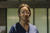 A woman wearing blue scrubs stands outside a medical building.