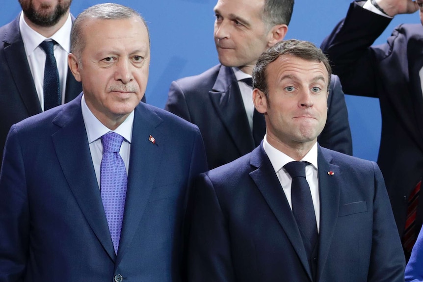 Turkey's President Recep Tayyip Erdogan, left and French President Emmanuel Macron stand in line in front of suited men.