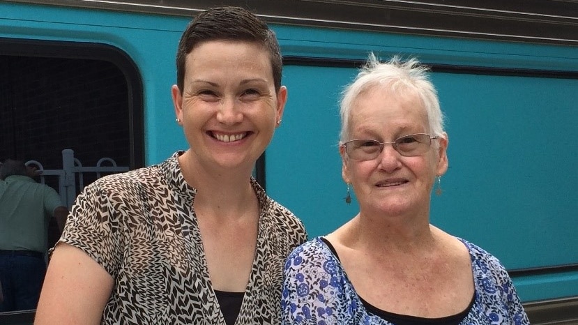 A woman stands next to an elderly woman and both smile at the camera