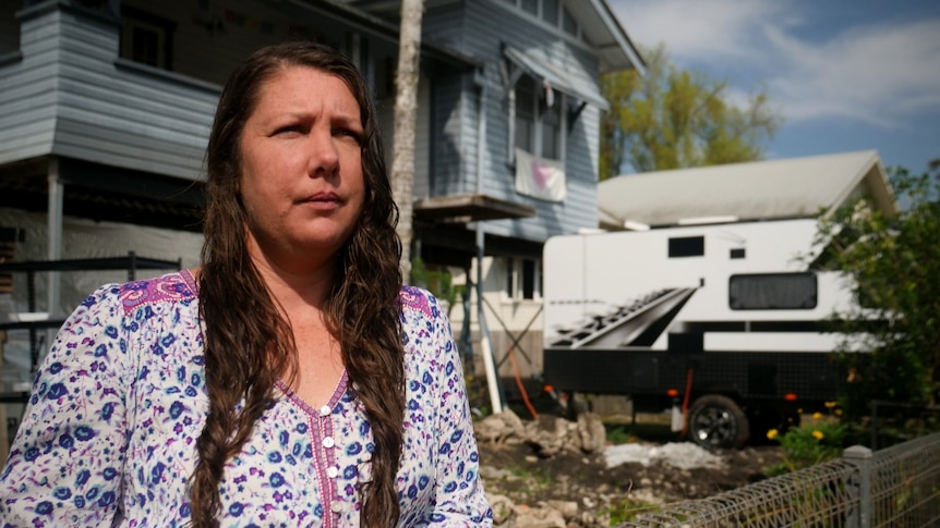 A woman with long brown hair in front of a house and caravan.