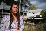 A woman with long brown hair in front of a house and caravan.