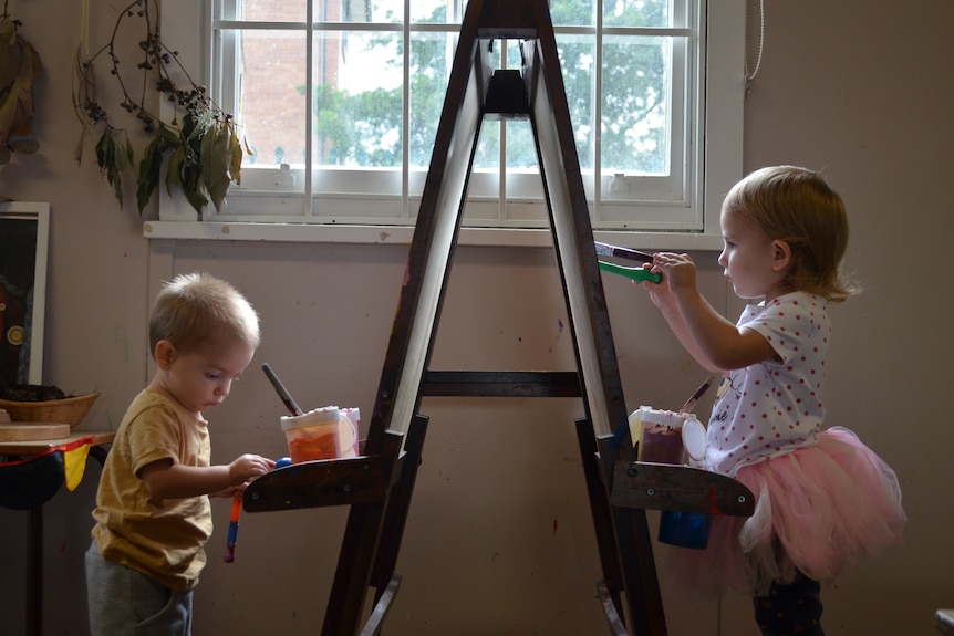 Two children paint infront of window facing each other