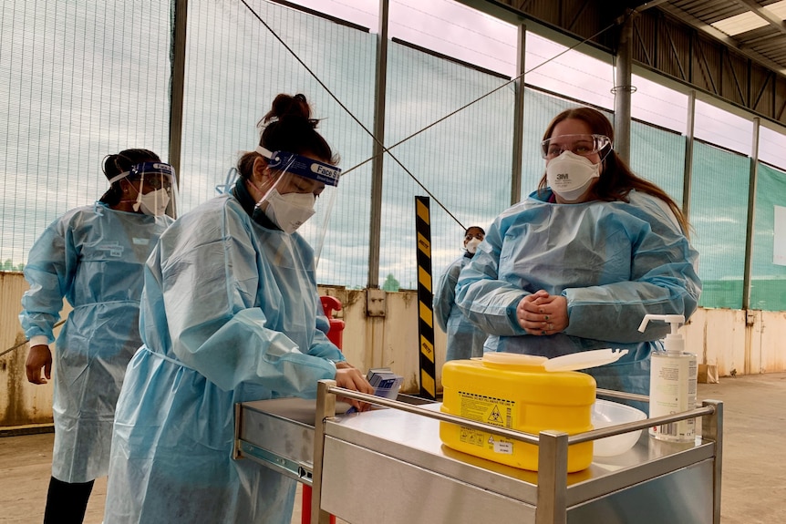 Nurses in full PPE prepare vaccines.