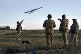 Soldiers stand around as a drone is launched by one of them into the air.