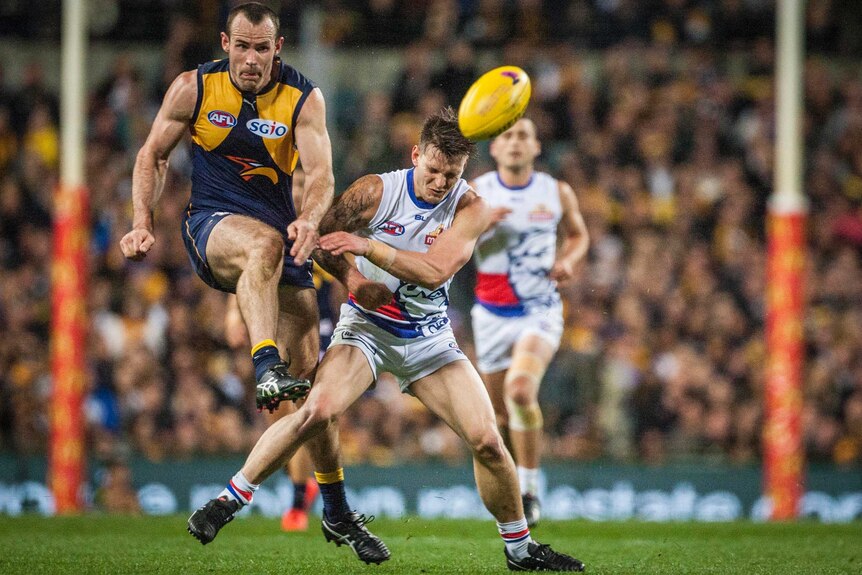 Shannon Hurn is bumped by Clay Smith as he kicks a football in an AFL match at Subiaco Oval.