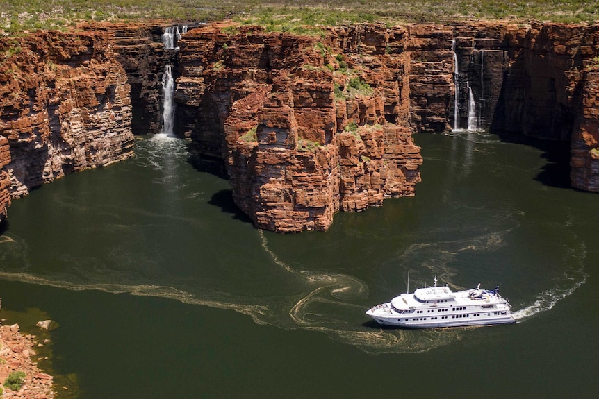 Image of a boat travelling up a river in a gorge with bushland on either side.