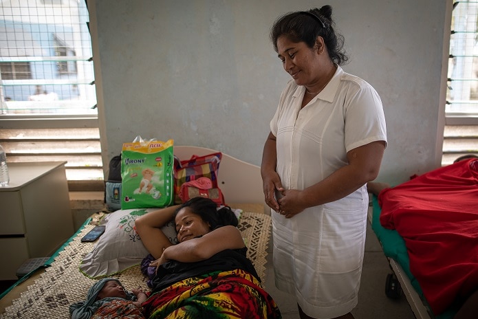 Midwife Makita looks down at a woman with her baby on a bed.