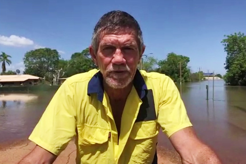 A man wearing yellow hi-vis sits on a boat in flooded streets