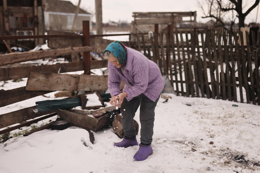 A woman stands in the snow and rubs her hands together, 