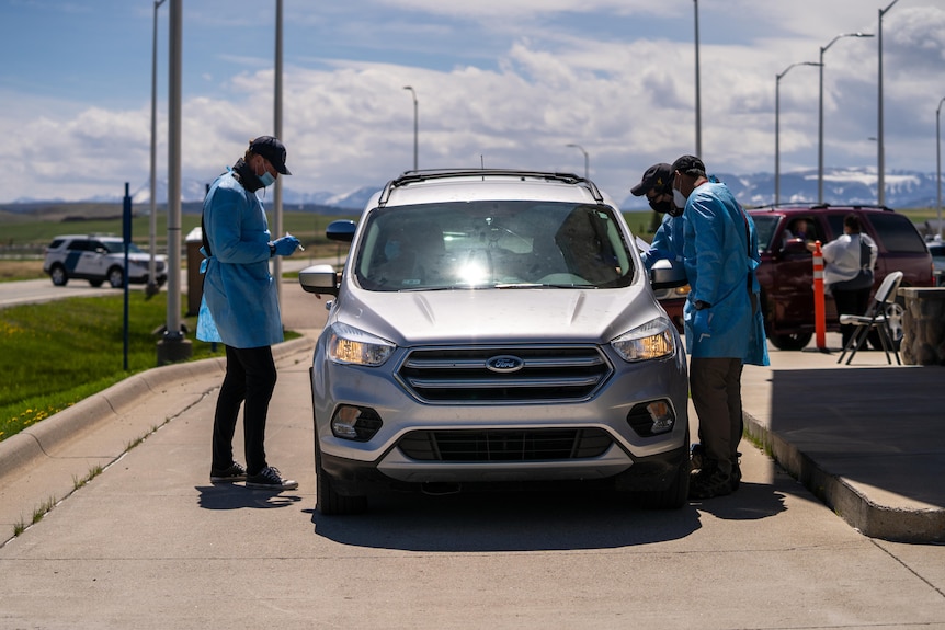 Health workers standing outside a car at a drive-through vaccine clinic.