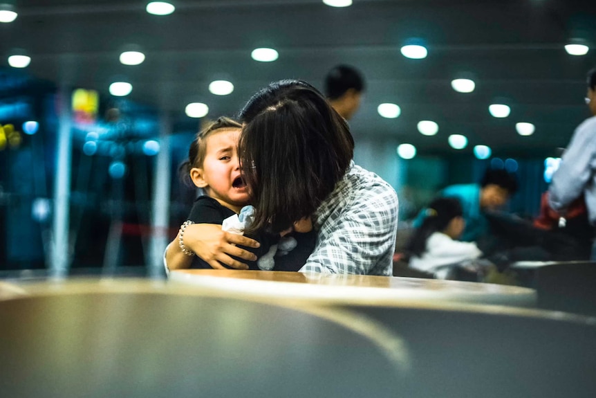 A little girl is comforted by her mother as she cries in a public area of an airport.