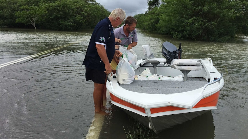 Two residents use a boat to take groceries, including beer, to family who are cut off by floodwaters in Townsville.