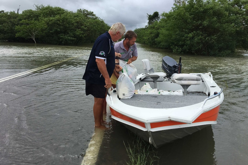 Two residents use a boat to take groceries, including beer, to family who are cut off by floodwaters in Townsville.